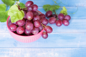 a bunch of grapes on a blue background close-up. pink grapes in a pink bowl on the table. background with a bunch of grapes and a vine.