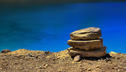heap of pebble stacked on lake shore with still blue waters in the background