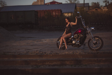 Fototapeta na wymiar Beautiful sexy woman in lace bodysuit and high heels sits on a motorcycle on an industrial background