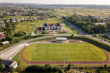 Aerial view of a football field on a stadium covered with green grass in rural town area. © bilanol