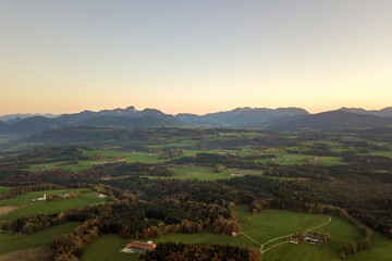 Naklejka premium Aerial view of small scattered farm houses with red tiled roofs among green farming fields and distant mountain forest in summer.