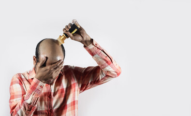 bald man covering his face and applying hair grow oil in white background with space for text