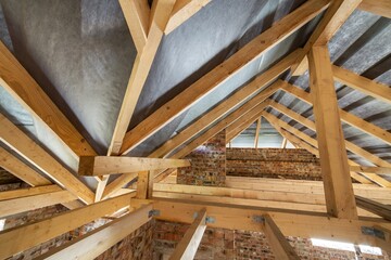 Attic of a building under construction with wooden beams of a roof structure and brick walls.
