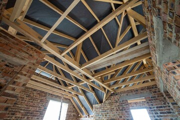 Attic space of a building under construction with wooden beams of a roof structure and brick walls. Real estate development concept.