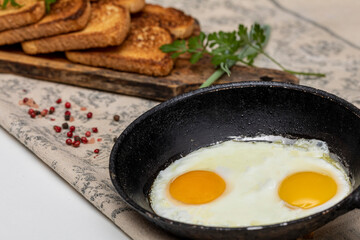 Fried eggs in a rustic iron pan, toast on a wooden board and a cup of coffee for breakfast.