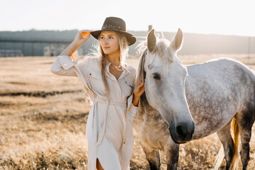 Young woman cowgirl with white horse standing at a farm.