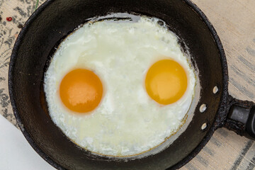 Fried eggs in a rustic iron pan for breakfast. Top view