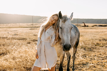 Young blonde woman with white horse standing in a field.