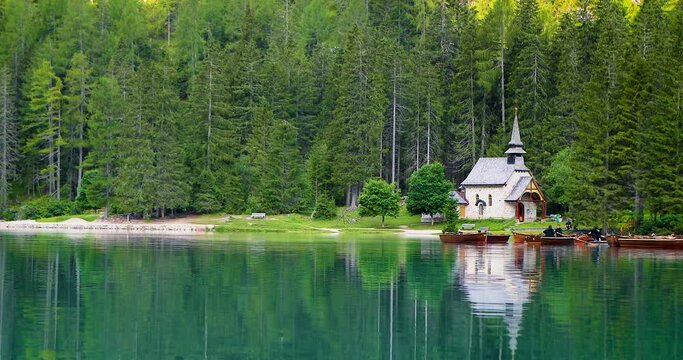 Church near a blue lake surrounded by green pine tree forest and mountains. Landscape view in 4K