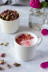 Pink moon milk with rose petals in white mug, healthy ayurvedic drink. Fresh rose and dried rose buds