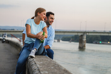 Young couple sitting on dock by the river  and joying in city view.