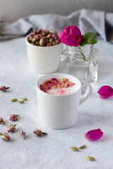 Pink moon milk with rose petals in white mug, healthy ayurvedic drink. Fresh rose and dried rose buds