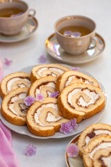 Tea time. Homemade roll cake with apricot marmalaid and cheese cream and two cups of tea. Decorated with pink flowers. 