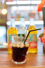 Big glass of alcohol drink on bar counter, beverage with straw with bottles of drinks on background, fresh cocktail for bar customers.
