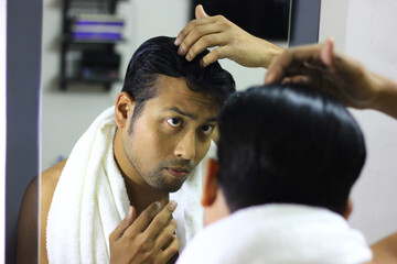 Obraz na płótnie Canvas indian asian man looking after his appearance in front of a mirror beauty styling lifestyle.hair styling