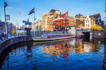 Monument to Queen Wilhelmina  on horse ,. pleasure(touristic) boat and water of canal and amazing medieaval architecture  of Amsterdam  Flag of the Netherlands