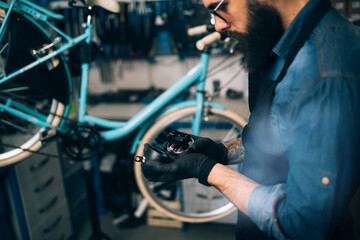 Young beard bicycle mechanic repairing bicycles in a workshop.