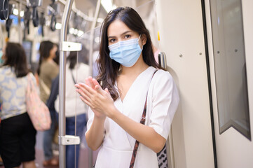 A young woman wearing protective mask in subway is using alcohol to wash hands, travel under...