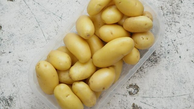 Fresh young potatoes in plastic basket placed on scatched rusty white background