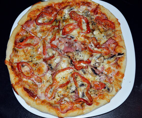 dish with pizza on a dark background. pizza with mushrooms, bell peppers, bacon and sausage