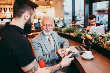 Mature businessman paying with contactless credit card with NFC technology.