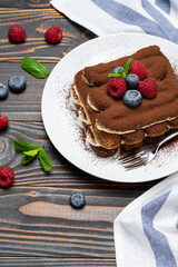 portion of Classic tiramisu dessert with raspberries and blueberries on wooden background