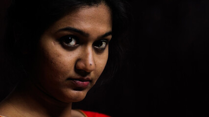 Fototapeta premium an indian female staring at the camera with thoughtful expression in black background with selective focus on rear eye