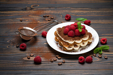 portion of Classic tiramisu dessert with raspberries on wooden background