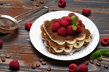 portion of Classic tiramisu dessert with raspberries on wooden background