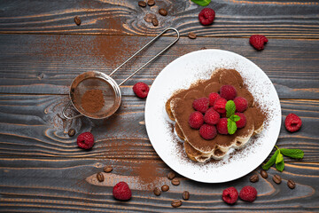 portion of Classic tiramisu dessert with raspberries on wooden background