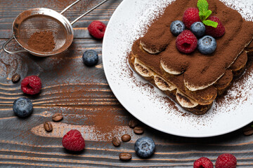 portion of Classic tiramisu dessert with raspberries and blueberries on wooden background