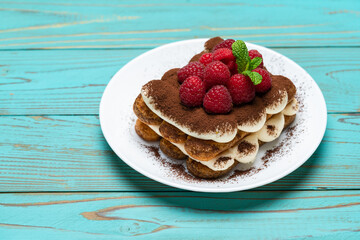 portion of Classic tiramisu dessert with raspberries on blue wooden background