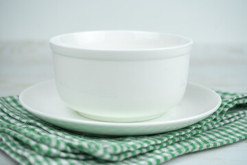 White empty ceramic bowl on a plate on a green kitchen plaid towel.