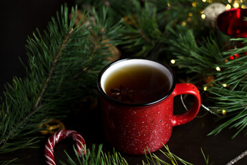 New year's tea party with spices. Red mug with tea surrounded by garlands, fir branches and spices