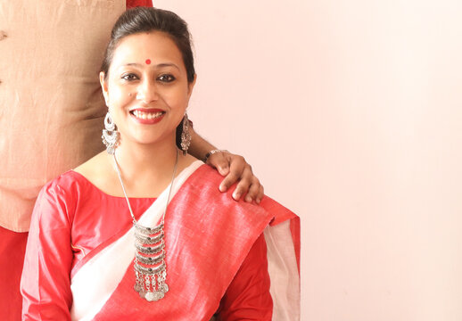 a young indian bengali assamese married lady dressed in red and white saree and smiling