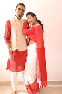 a young indian bengali assamese married romantic couple dressed in red and white ethnic indian dress, looking at the camera and smiling