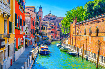 Venice cityscape with narrow water canal with moored boats between old colorful multicolored buildings and stone promenade, Veneto Region, Northern Italy. Typical Venetian view, blue sky background.