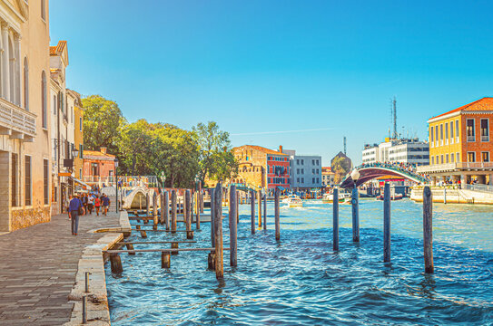 Venice cityscape with Santa Croce stone promenade, pier with wooden poles in water, yachts sailing Grand Canal waterway, Ponte della Costituzione Constitution bridge, Veneto Region, Italy