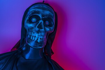 Close up view of blue lighted skeleton head on purple background. Halloween concept.
