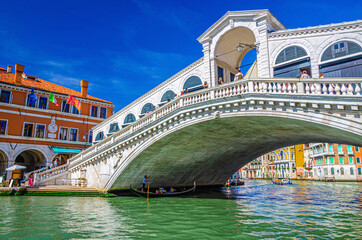 Fototapeta na wymiar Venice cityscape with Rialto Bridge across Grand Canal waterway, Venetian architecture colorful buildings, gondolas boats sailing Canal Grande, blue sky in sunny day. Veneto Region, Northern Italy.