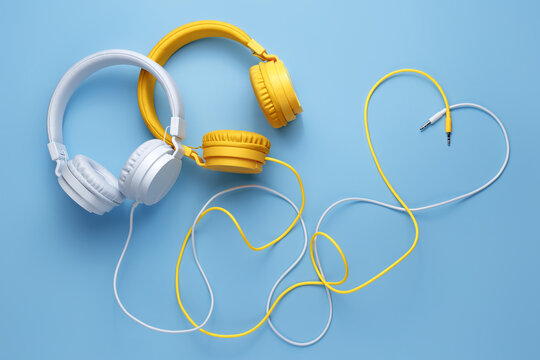 Pretty image of two headphones whit cables in heart shape over blue background. Music concept.