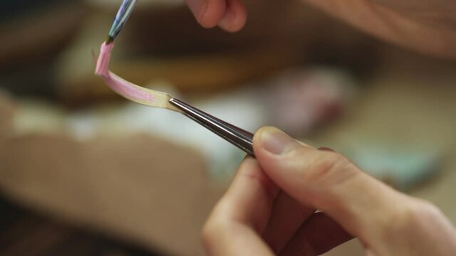 Man uses brush to put oil paint pink color on small piece of paper
