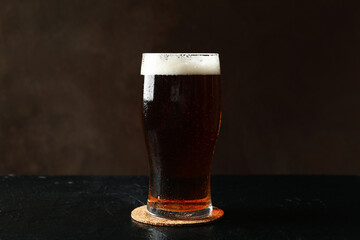 Glass of beer on black table against brown background