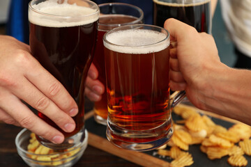 Four men cheers with beer on wooden background with snacks