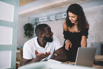 Positive dark skinned male and female colleagues discussing ideas ponting on web page, smiling african american couple in love talking about online shopping share ideas and using laptop computer