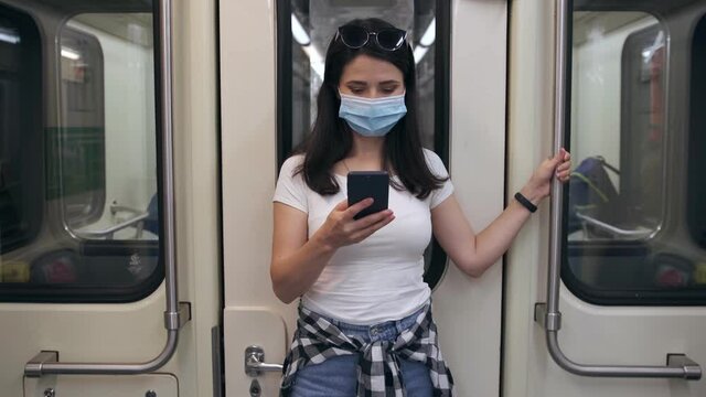 A young, modern woman rides in a protective medical mask with a phone on the subway and holds on to the handrail. The concept of protection and prevention from viral diseases. Coronavirus pandemic.