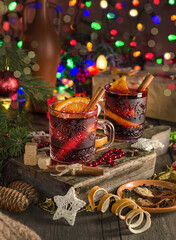 Mulled wine with orange slice, cinnamon stick on the background of festive garland lights. Dark style
