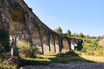 Fototapeta na wymiar Panorama view of ancient bridge. Viaduct with old railway tracks near green hill of mountain forest. Locat travel concept