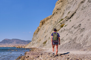 Fototapeta premium A tourist walks along the path of the rocky coast of Cape Meganom on the Black Sea, Crimea peninsula.