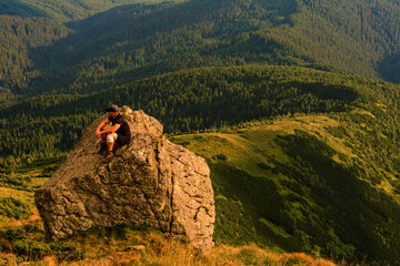 A tourist sits on a rock and looks into the distance, photos on top of Mount Pip Ivan Chornohirsky,...